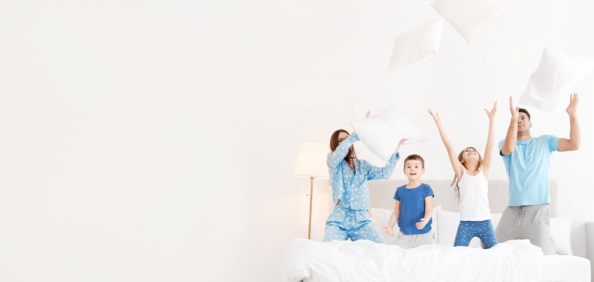 Family of four on a bed tossing the pillows in the air, playing